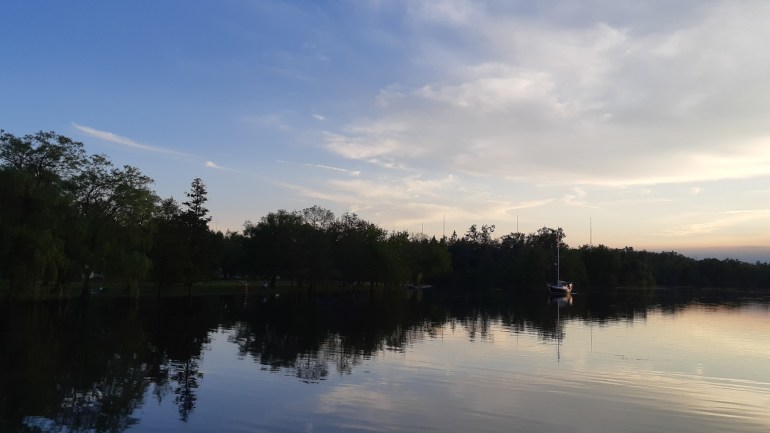 Sunset in the Toronto Islands, dark silhouette of trees along a river bank against a blue evening sky with small yacht on river